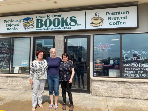 Three colleagues smiling outside of used bookstore storefront