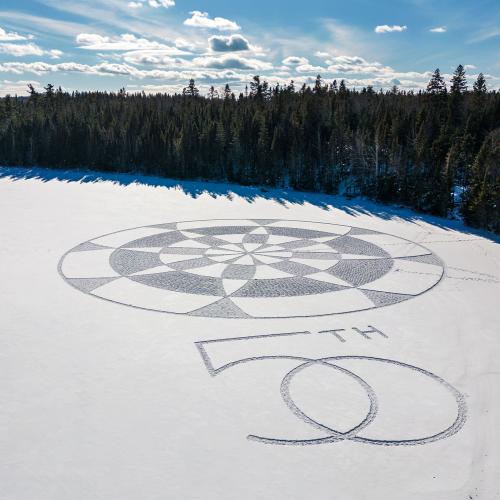 Snowshoe Art in the shape of 50th anniversary logo on lake surrounded by trees