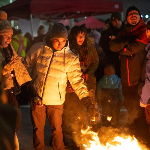 A group of people around an open fire roasting marshmallows in the winter