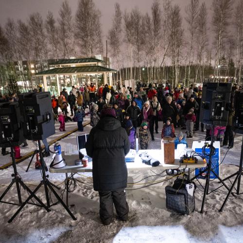 A crowd of people facing a DJ booth on a snowy night