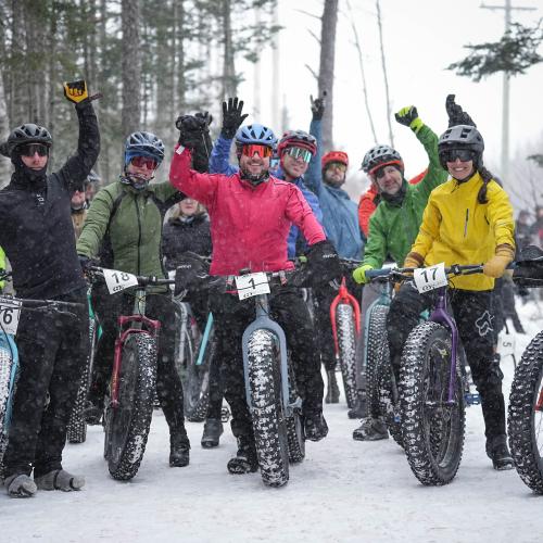 A group of people on fat bikes smiling at the camera in the winter