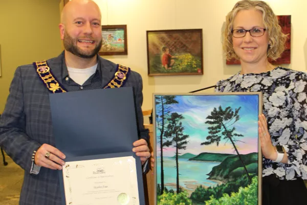 Artist holding painting of a tree over water with mayor