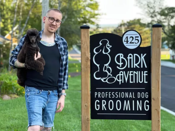 Owner of Bark Ave Grooming holding dog by business sign
