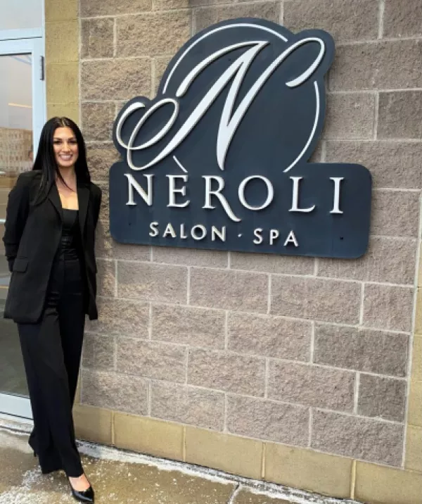 Owner of neroli spa standing next to sign outside business