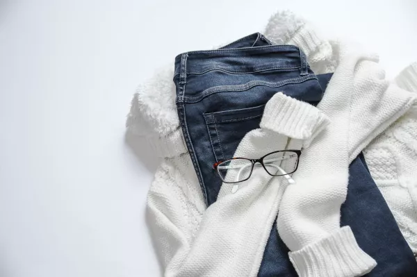 A white sweater, jeans, and a pair of glasses in a pile 