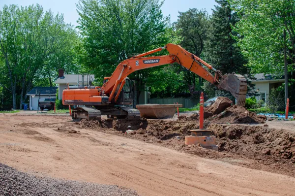 An orange excavator digging in dirt on a road