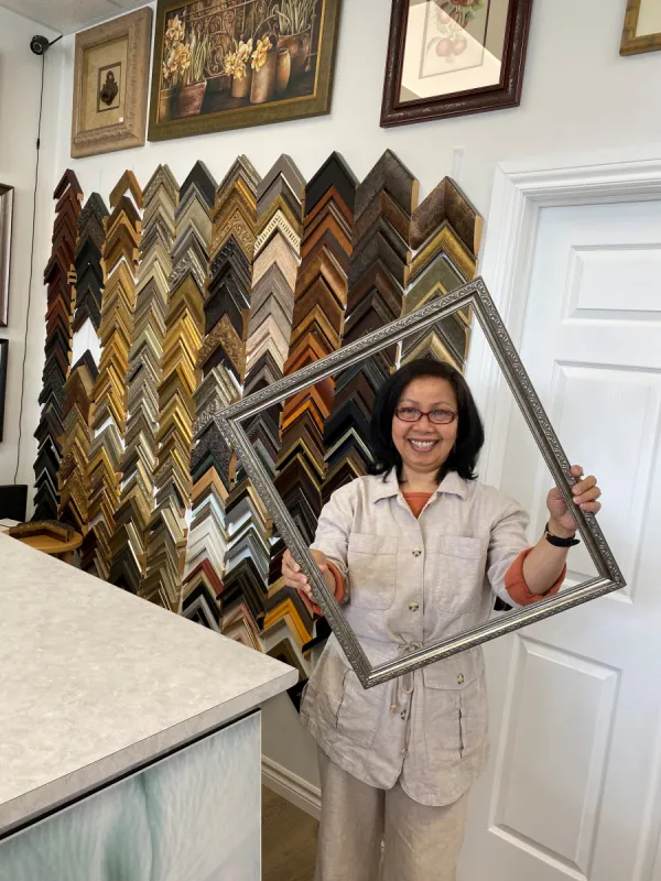 Owner of Kay's Custom Framing smiling holding an empty picture frame
