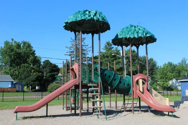A playground with trees in the background and a blue clear sky located on Hawthorne Drive. 
