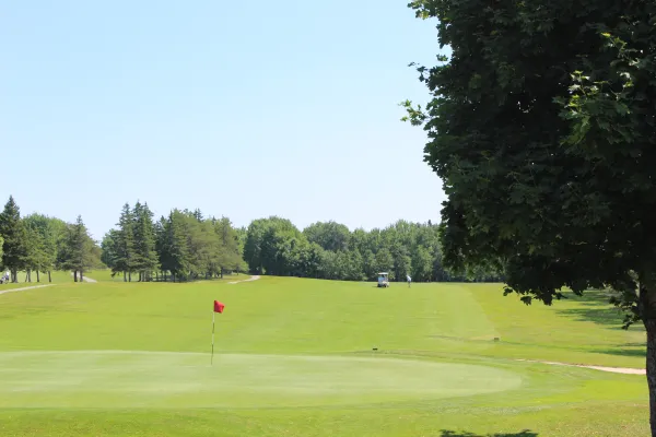 Golf course view from Spruce & Iron. Green lawn with trees in distance and a red golf flag.