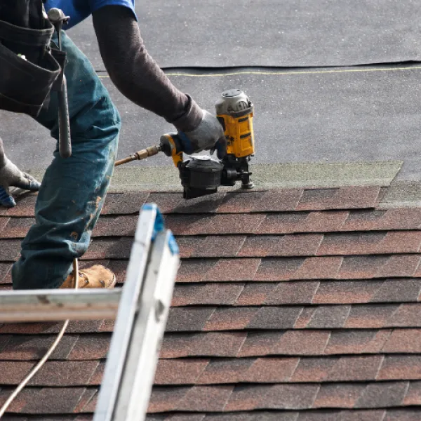 Worker attaching roof shingles with power tool