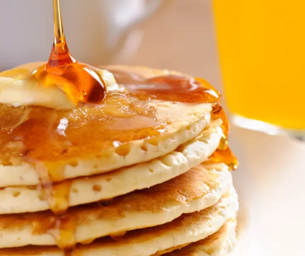 A stack of fluffy pancakes with maple syrup pouring over top