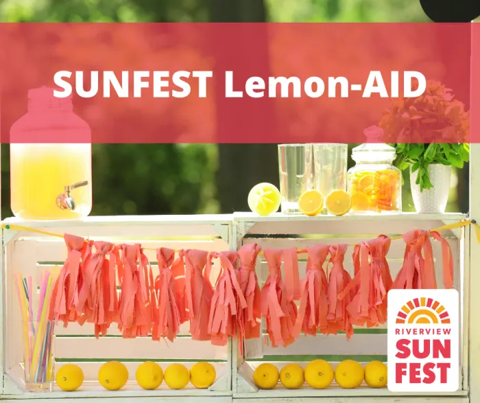 photo of a lemonade stand with a red banner overtop that reads "SUNFEST Lemon-AID" with the Riverview Sunfest logo on the bottom right of the image