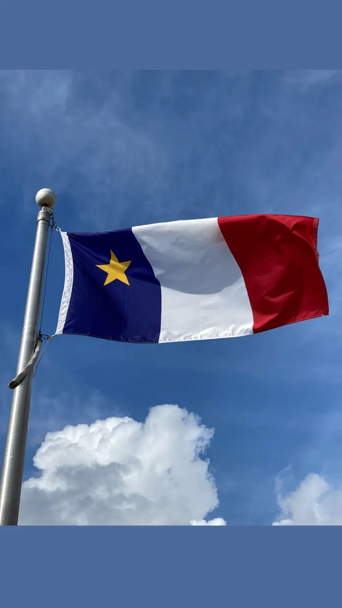 Acadian flag flying in front of a blue sky at Town Hall 