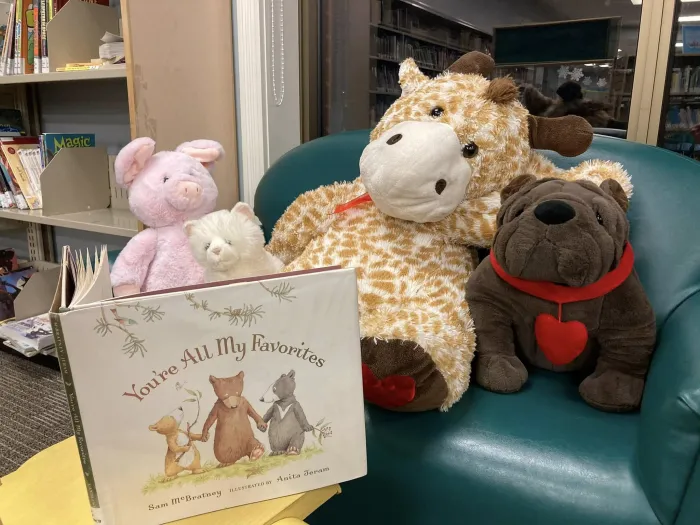 Stuffies sitting on a chair reading a book at the library