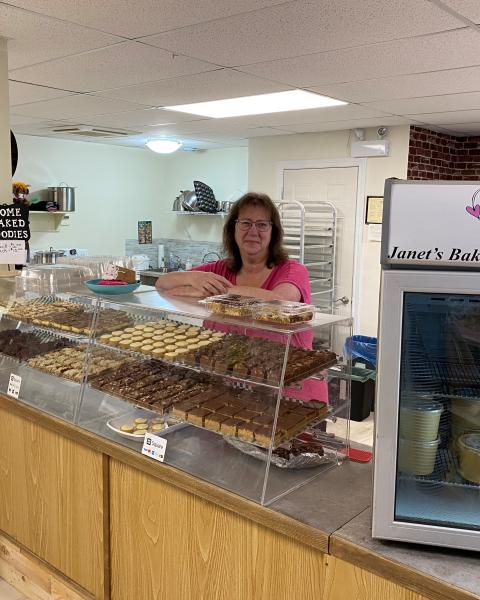 Janet inside her bakery standing behind the display case