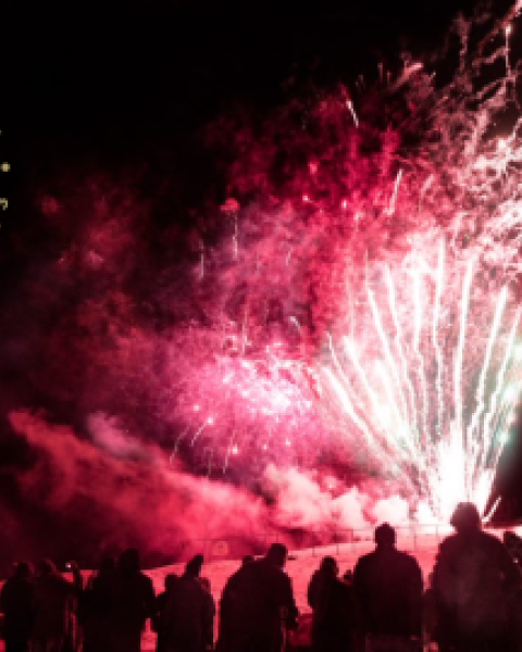 Crowd of people watching fireworks glowing red in the wintertime