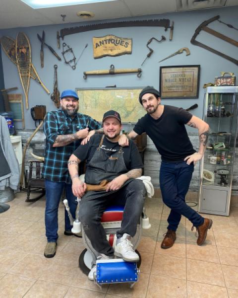 Barber sitting in barber chair with colleague on either side 