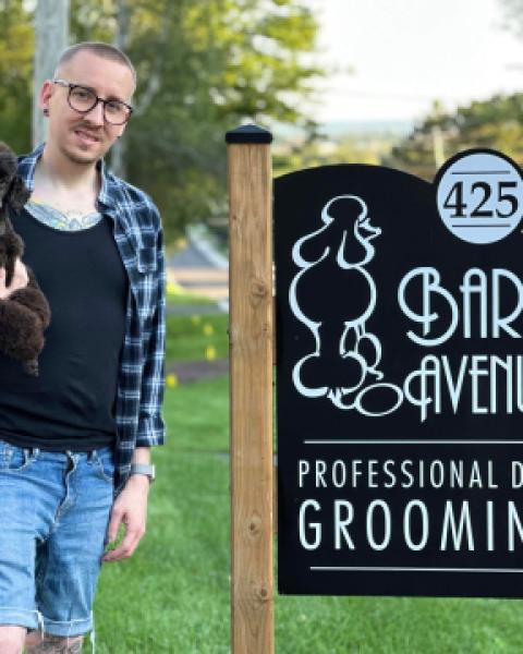 Owner of Bark Ave Grooming holding dog by business sign