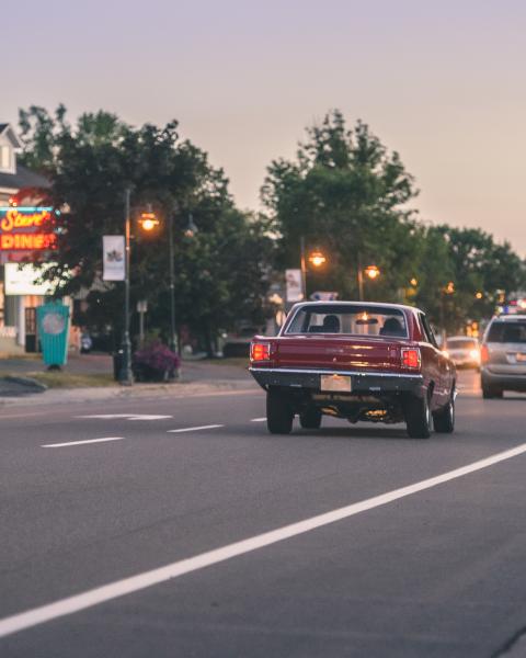 Vintage car driving away down a road at dusk