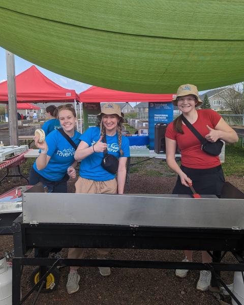 Three students running a BBQ in the community garden