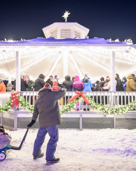 Gazebo lit up with holiday lights and people gathered.