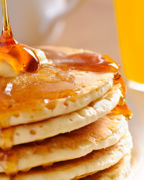 A stack of fluffy pancakes with maple syrup pouring over top